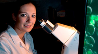 !Image shows student smiling as she prepares to use a high-powered microscope. 