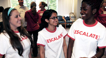 Three female students talking and smiling while wearing ESCALATE t-shirts.