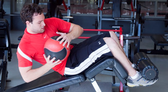 !Image shows male student exercising with a medicine ball while doing sit ups in the lifting room.