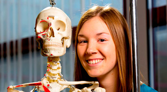 !Student poses with the model of a human skeleton.