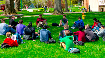 !Students sit in the grass in Root Quadrangle on a sunny day.
