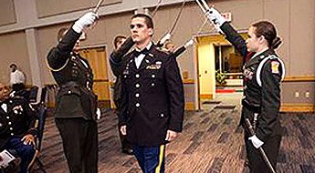 Man in uniform walks as others in uniforms raise their swords above him.