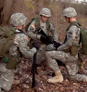 Group of three men in uniform huddle outside with their weapons.