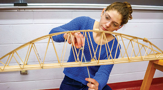 !Female student testing engineering bridge project.