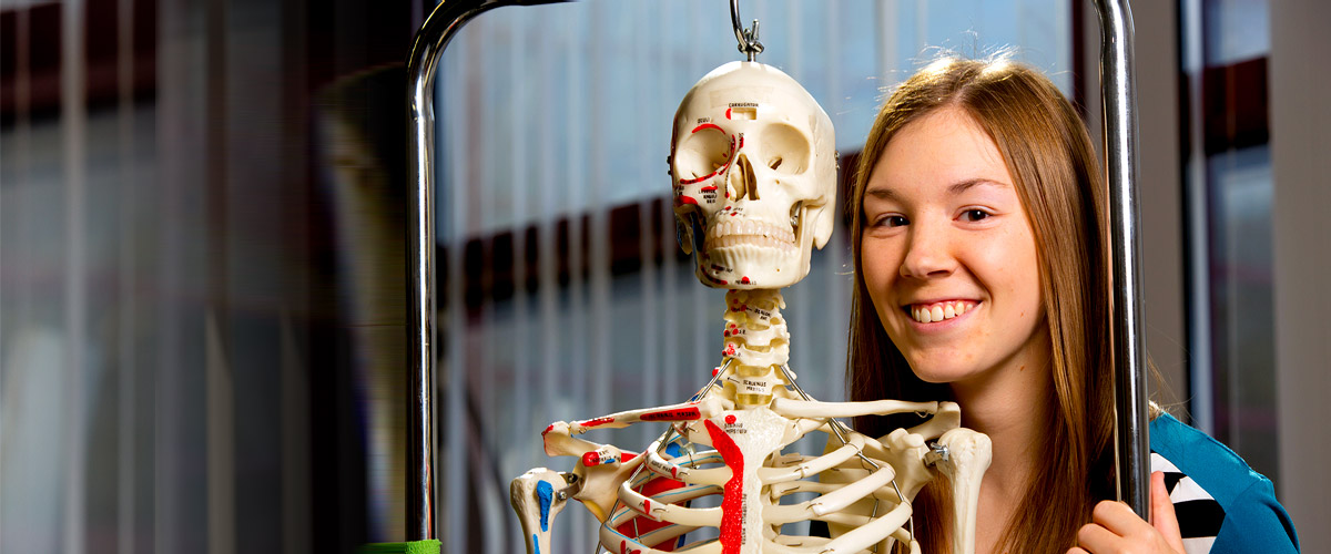 Biology student posing for photograph alongside a human skeleton.