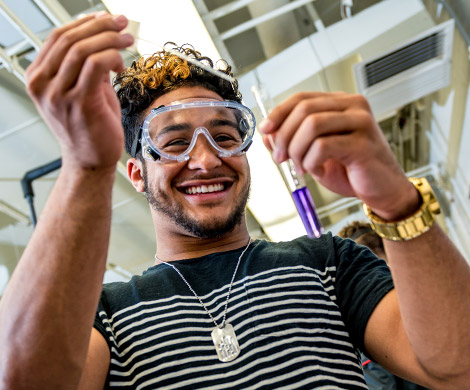 Smiling male student adds liquid to a test tube.