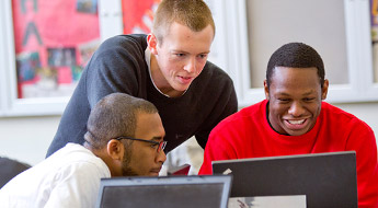 A group of male students smile as they look at a computer screen.