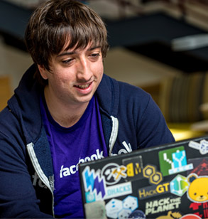 Student smiling while working at a laptop computer that is covered in colorful stickers.