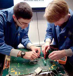 Two male students test circuit board.