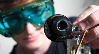 Male student wearing goggles adjusts optics device.
