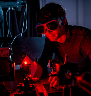 Man wearing goggles works with red laser in darkened lab.