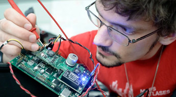 A male student carefully soldering a wire to a circuit board.