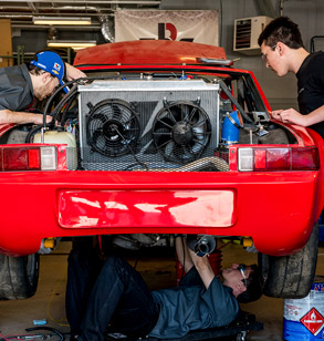 Three male students work on a red car.