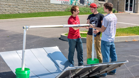 Three male students stand near solar oven project.