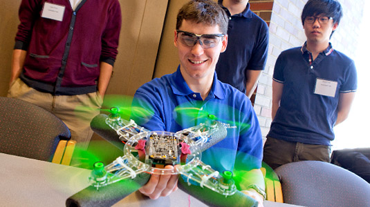 Student holds an aerial drone with spinning green propellers.