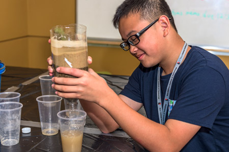 Male student holds upside-down two-liter bottle filled with layers of sand to make a water filter.