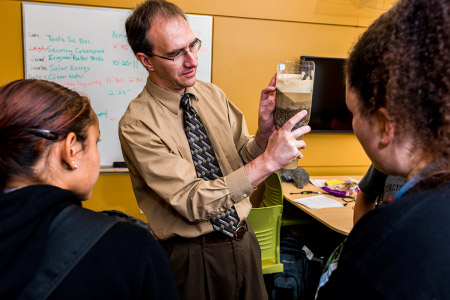 Professor demonstrates water filtration using an upside-down two-liter bottle filled with layers of sand to make a water filter.