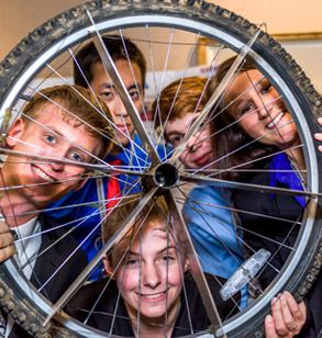 Students looking through a spoked wheel.