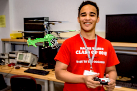 A male Catapult student smiling broadly while operating a flying remote-controlled helicopter.