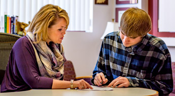 Image shows a financial aid employee helping a student complete the paperwork needed to apply for financial assistance.