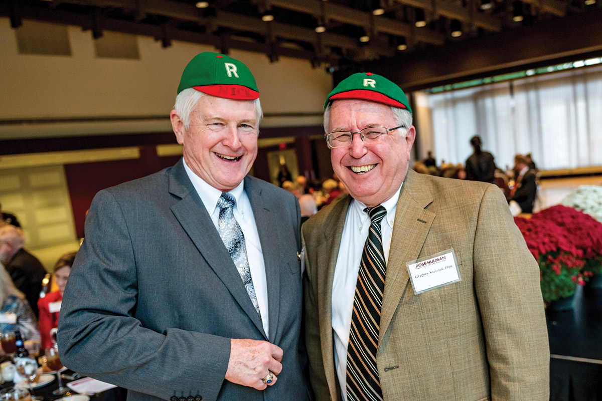 Older male alumni wearing beanies smile for the camera