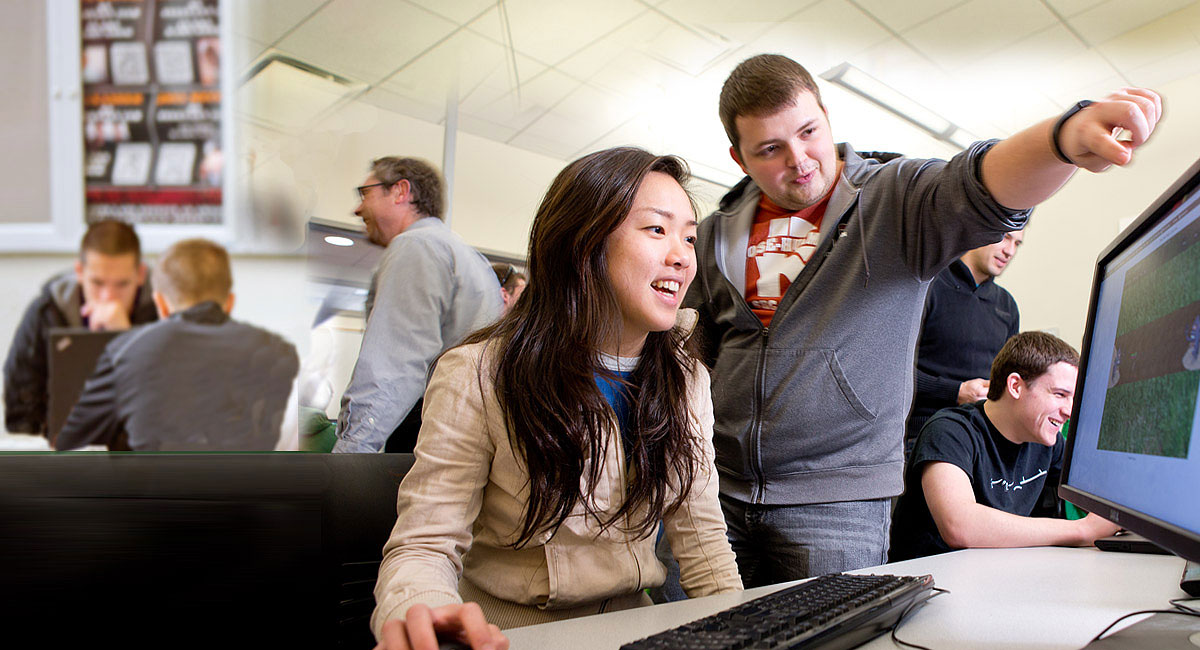 Male student points at a computer screen while smiling female student looks on.