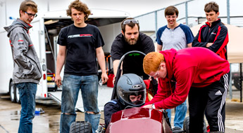 !Several members of the Rose Grand Prix Racing team help the team’s driver prepare for a race.