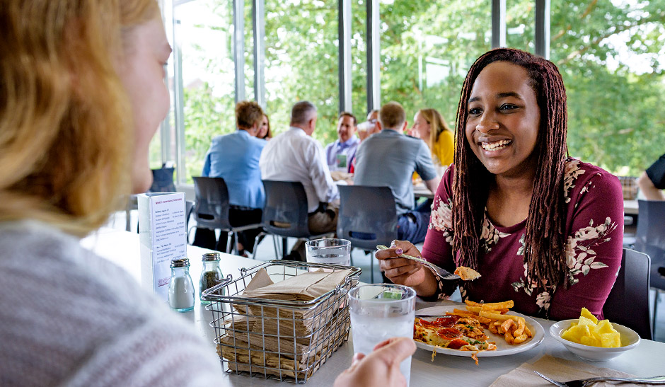Two female students laugh and talk during a meal in the student union.