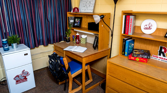 Desk, dresser, and a mini fridge in a room in Speed Hall.