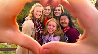 !Members of the Panhellenic Council smiling and framed by two hands making a heart shape.