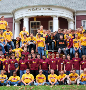 A large group of the members of Pi Kappa Alpha pose in several rows in front of their pillared fraternity house
