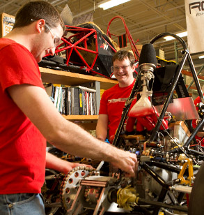 Two male students working on  the Rose-Hulman Formula SAE race car inside  the Branam Innovation Center. 