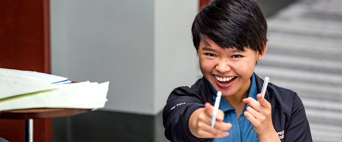 Smiling female student pointing at the camera.