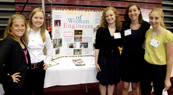 Female students stand beside Society of Women Engineers display board.