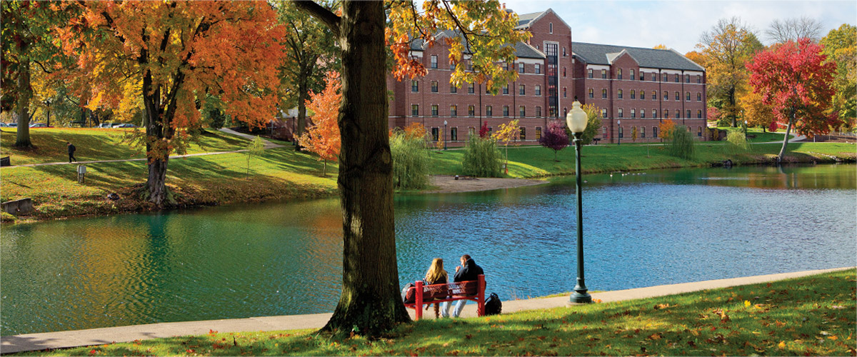 Students relax on a bench near Speed Lake on an autumn day at Rose-Hulman.