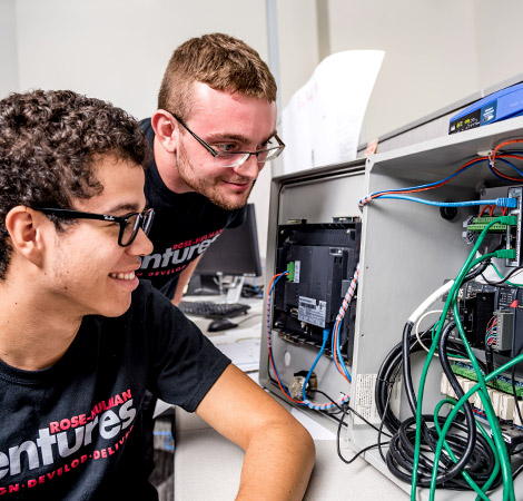 A pair of smiling male students at Rose-Hulman look at a series of network cables in the Ventures location