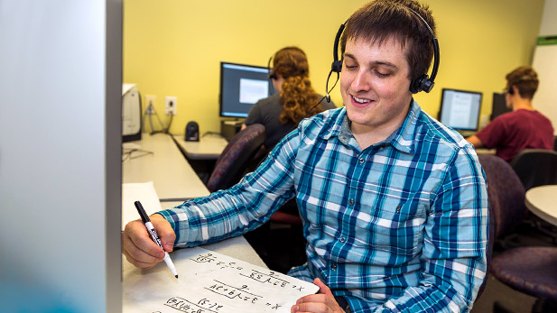 Female student tutor working out a math problem while taking a phone call at the Homework Hotline.