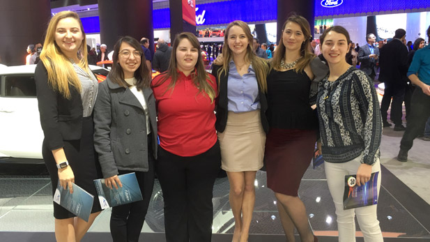 Female students posing in a prop car cut-out at North American International Auto Show (NAIAS) in Detroit, Mich.