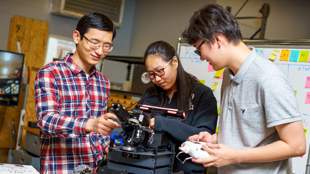 Three students pose with the robotic device they programmed for the  Robomaster challenge.