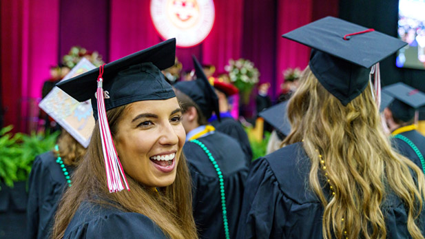 A female Rose-Hulman student in commencement gear smiles as she prepares to receive her diploma.