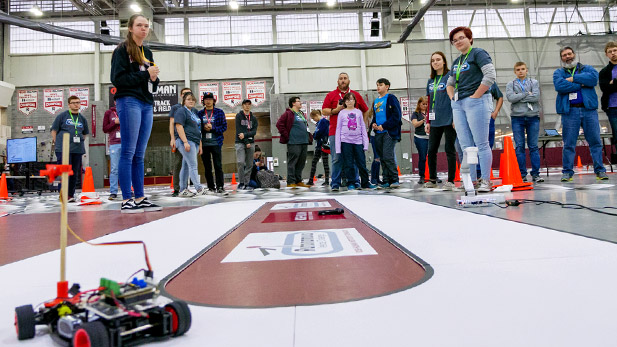 Student competitors watch as autonomous vehicles navigate a track