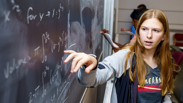 Female student gesturing toward equations on a chalk board