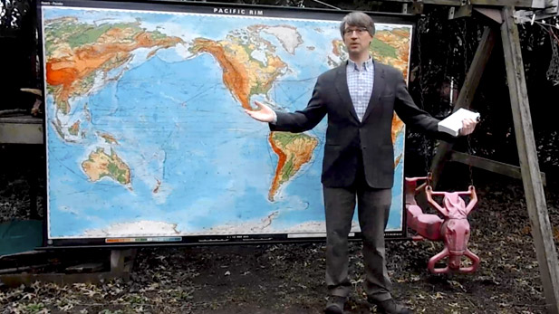 Professor Martland standing in front of a world map attached to a children's swing set.
