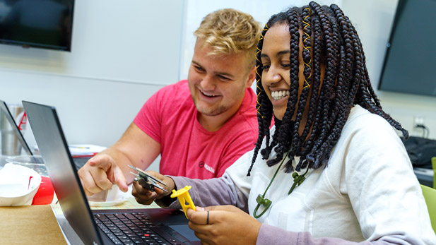 Image shows male and female students smiling and working on a project together.