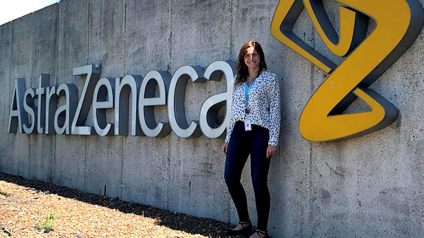 Image shows a smiling Madison Wendelin standing outside next to a sign reading AstraZeneca.