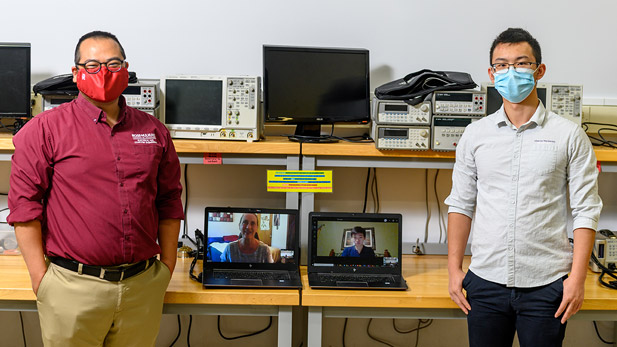 Professor Michael Jo and a student pose next to computers while they are involved in a tele-meeting with other researchers.