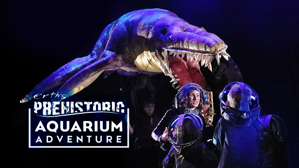 Performers and aquatic dinosaur puppets on stage.