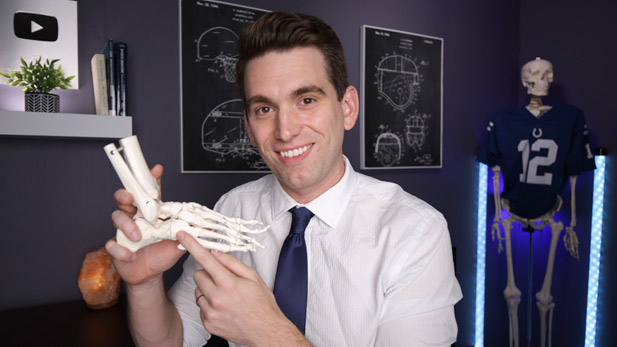 Image shows Brian Sutterer smiling and holding a human foot skeleton and pointing to the bones.