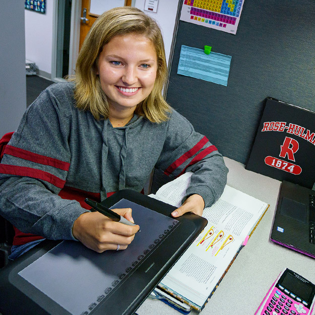 Image shows student employee of AskRose talking on the phone while consulting a textbook to help a student caller.