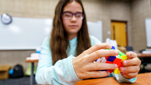 Image shows young girl working a Rubic's Cube.
